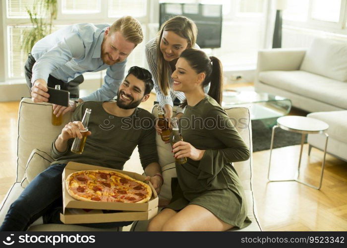 Group of young people eating pizza, drinking cider and watching tablet in the room