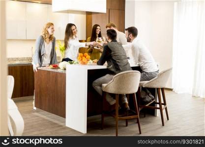 Group of young people having dinner and drinking wine in the modern kitchen