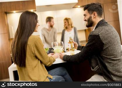 Group of young people having dinner and drinking wine in the modern kitchen