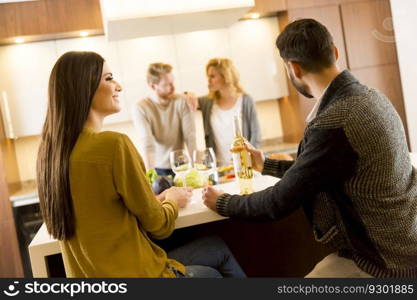 Group of young people having dinner and drinking wine in the modern kitchen