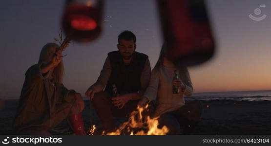 Group of young people having fun at beach around bonfire on sunset