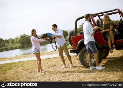 Group of young people having fun by cabriiolet car on the bank of the river