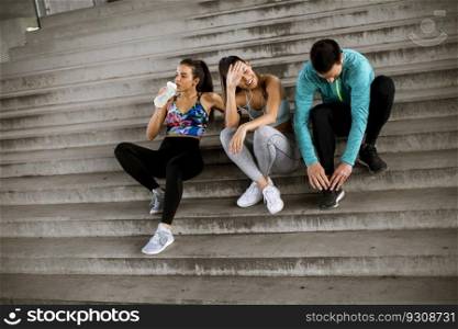 Group of young people resting during training with bottle of water in urban environment