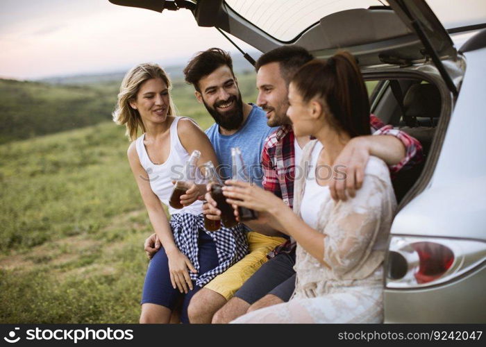 Group of young people sitting in the car trank during trip in the nature