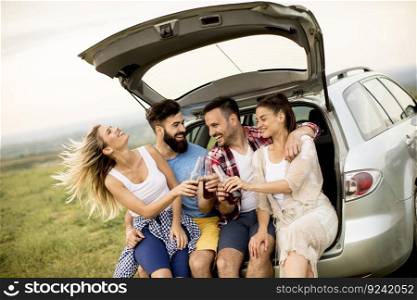 Group of young people sitting in the car trank during trip in the nature