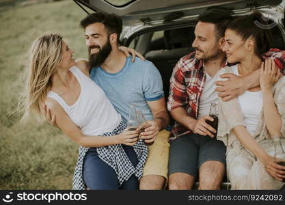 Group of young people sitting in the car trank during trip in the nature