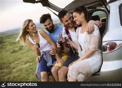 Group of young people sitting in the car trank during trip in the nature