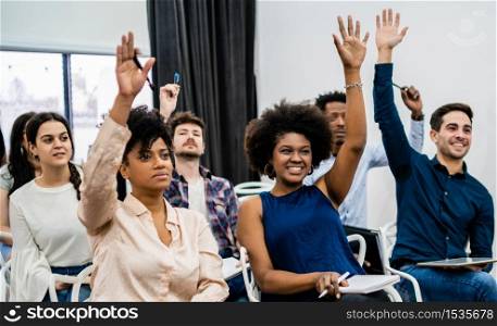 Group of young people sitting on conference together while raising their hands to ask a question. Business team meeting seminar training concept.