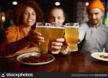 Group of young people smiling at camera and clinking glasses. Happy multiracial friends toasting with beer. Meeting in sports bar. Group of young people smiling at camera and clinking glasses