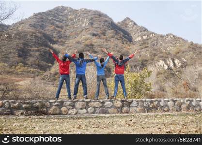 Group of young people standing on the ledge, arms outstretched