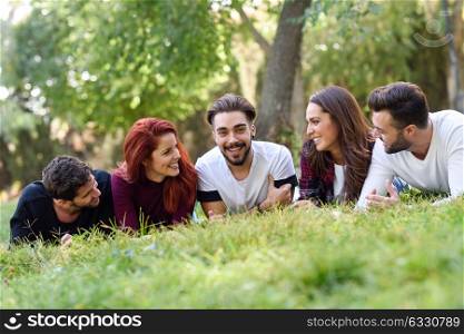 Group of young people together outdoors in urban park. Women and men laying on grass wearing casual clothes.