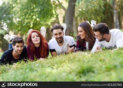 Group of young people together outdoors in urban park. Women and men laying on grass wearing casual clothes.