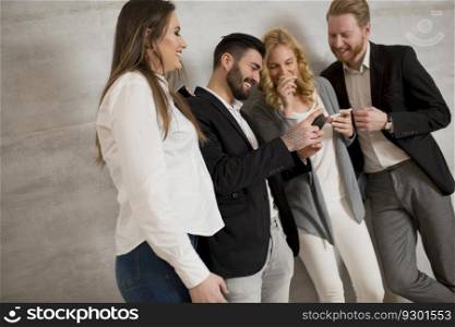 Group of young people with mobile phones standing by the grey wall