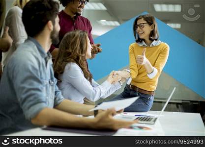 Group of young startup coworkers interacting around a table and handshaking in the office