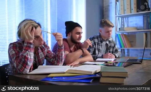 Group of young teenagers sitting in classroom and taking notes in notebooks with pen and pencil. Students studying together at the university. Stylish hipsters learning at college.