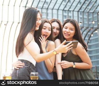 group of young women friends having fun looking at something funny on their smart phone and laughing while having party on rooftop night club