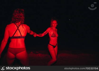 Group of young women having fun at a lakeside party at night with a red light