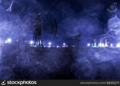 Group oil rigs and brightly lit industrial site at night. Raindrops texture. Through wet glass. Toned blue.