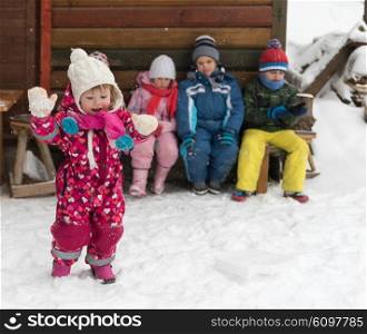 group portrait of kids, little child group sitting together in front of wooden cabin on vacation at beautiful winter day with fresh snow