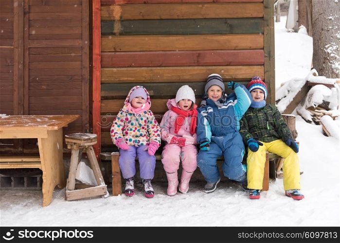 group portrait of kids, little child group sitting together in front of wooden cabin on vacation at beautiful winter day with fresh snow