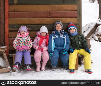 group portrait of kids, little child group sitting together in front of wooden cabin on vacation at beautiful winter day with fresh snow