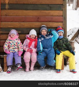 group portrait of kids, little child group sitting together in front of wooden cabin on vacation at beautiful winter day with fresh snow