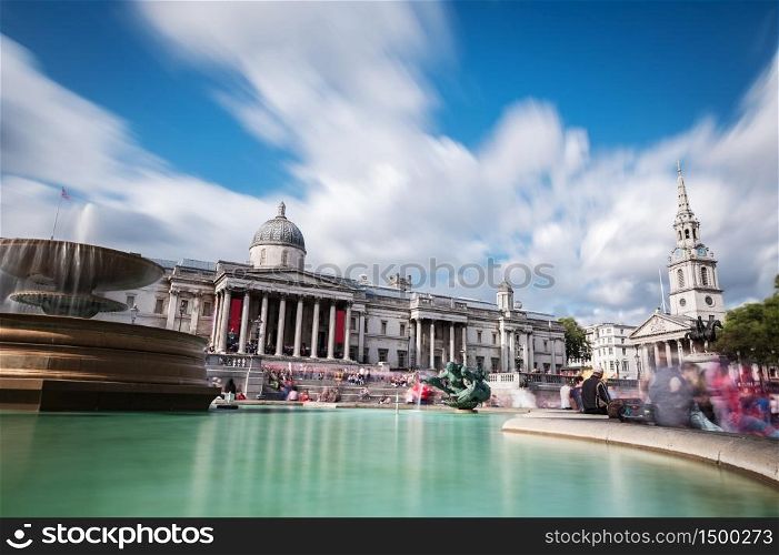 Groups of tourists and locals enjoy the sunshine at the main entrance to the National Gallery in Trafalgar Square. The gallery houses the national collection of western European painting. Long exposure.