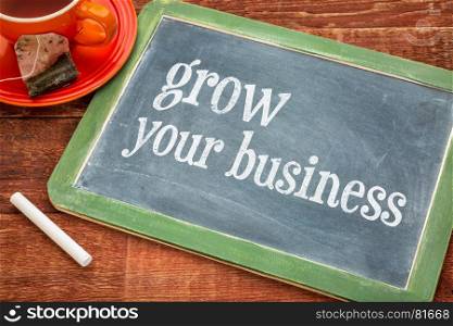 grow your business - motivational text on a slate blackboard with chalk and cup of tea