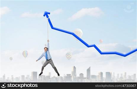 Growing graph. Young businessman hanging on increasing blue graph