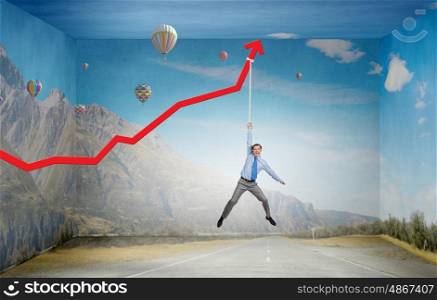 Growing graph. Young businessman hanging on increasing red graph