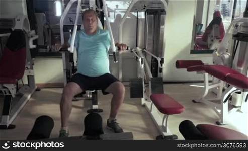 Grown man in gym sitting on the exerciser and performs exercises chest press