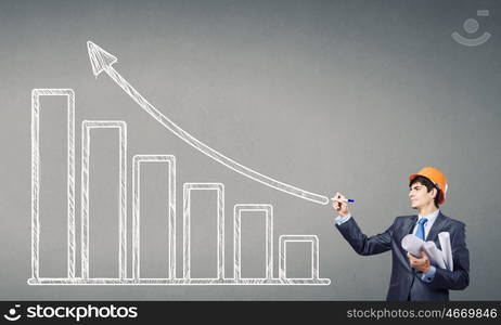 Growth and progress. Young man engineer in helmet drawing increasing graph