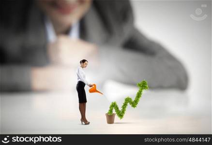 Growth concept. Businesswoman looking at miniature of woman watering plant