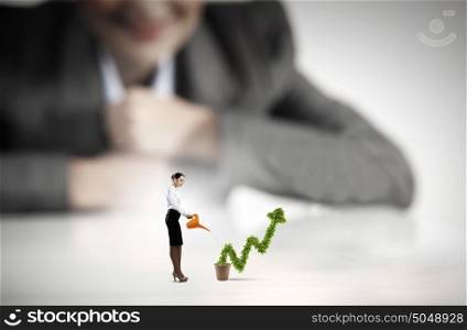 Growth concept. Businesswoman looking at miniature of woman watering plant