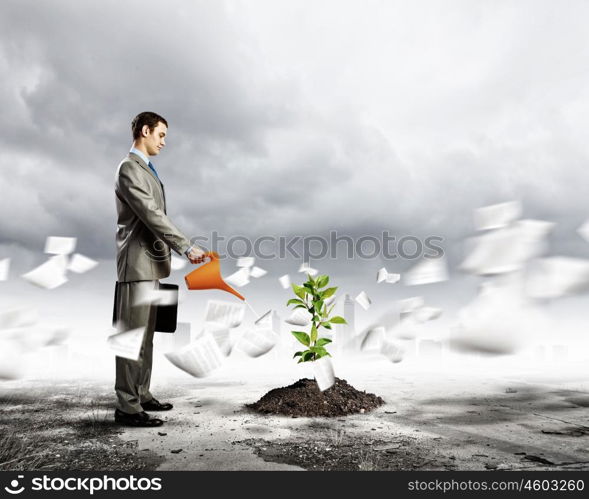 Growth concept. Image of businessman watering sprout with can