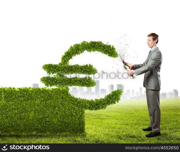 Growth concept. Young businessman cutting bush in shape of euro symbol