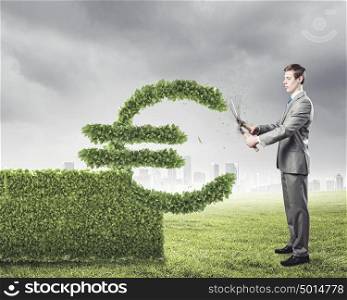 Growth concept. Young businessman cutting bush in shape of euro symbol