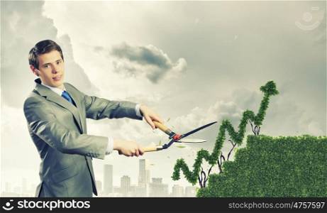 Growth concept. Young businessman cutting bush in shape of graph