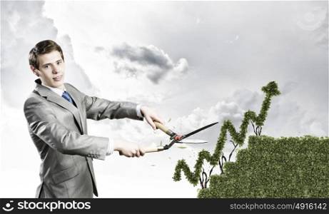 Growth concept. Young businessman cutting bush in shape of graph
