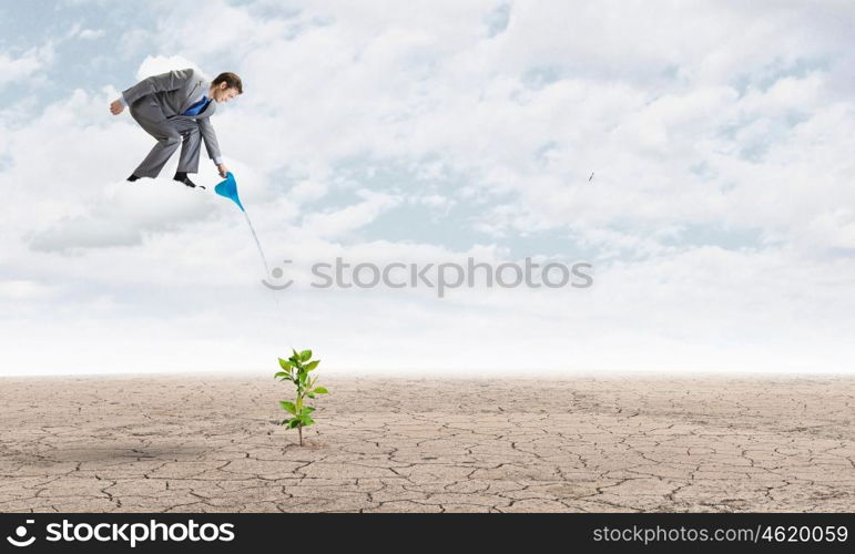 Growth concept. Young businessman standing on cloud and watering sprout