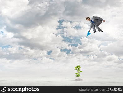 Growth concept. Young businessman standing on cloud and watering sprout