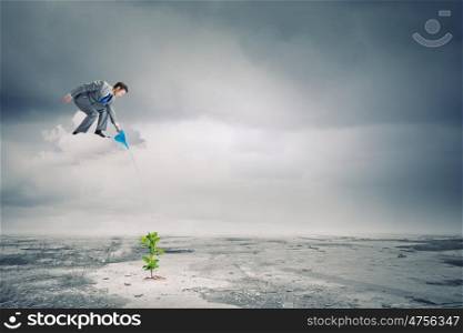 Growth concept. Young businessman standing on cloud and watering sprout