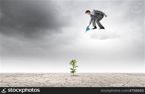 Growth concept. Young businessman standing on cloud and watering sprout