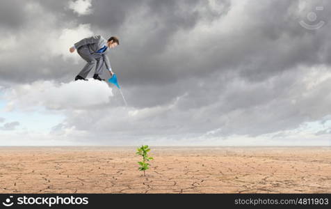 Growth concept. Young businessman standing on cloud and watering sprout