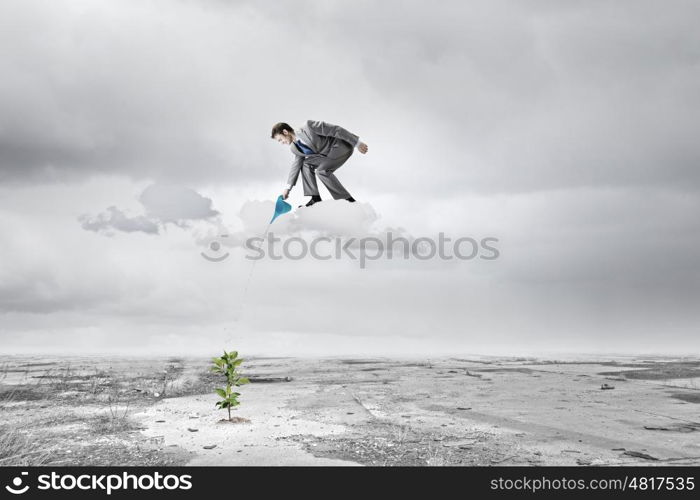 Growth concept. Young businessman standing on cloud and watering sprout