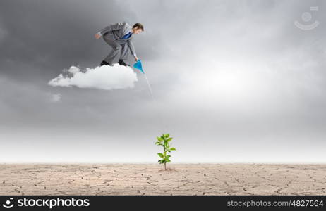 Growth concept. Young businessman standing on cloud and watering sprout