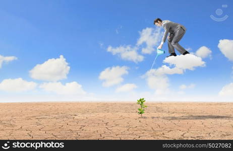 Growth concept. Young businessman standing on cloud and watering sprout