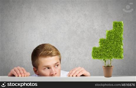 Growth concept. Young man looking out on tree in pot from under the table