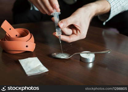 Grug addict man gathers a dose of heroin in syringe.