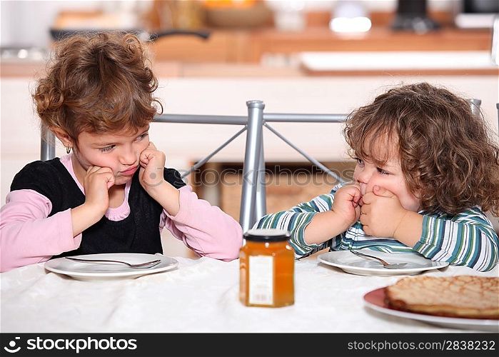 Grumpy children at a table with pancakes
